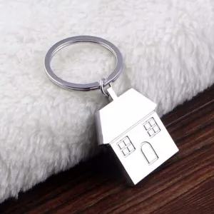 Polished silver house-shaped metal keychain on a soft white plush and wooden surface