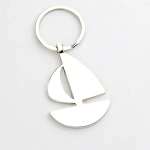 Polished silver metal sailing boat keychain with minimalist cutout design on white background