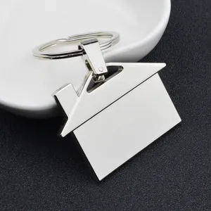Polished silver house-shaped metal keychain with a minimalist home pendant on white ceramic