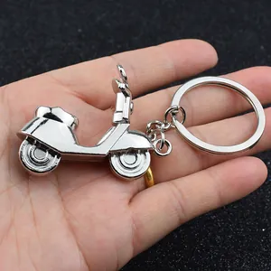 Handgehaltener silberner Metall-Motorroller-Schlüsselanhänger vor dunklem Hintergrund