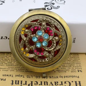 Vintage bronze hollow folding makeup mirror with colorful rhinestones on a retro background