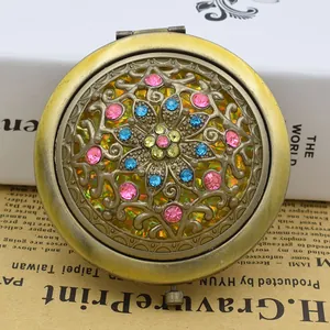 Close-up of vintage bronze compact mirror with filigree cutout and colorful rhinestones