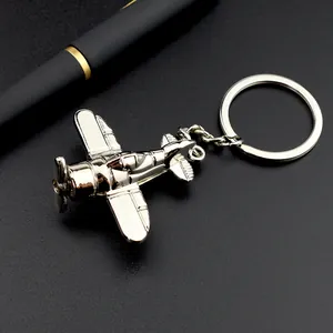 Porte-clés avion à hélice vintage en métal argenté sur fond noir avec un stylo élégant