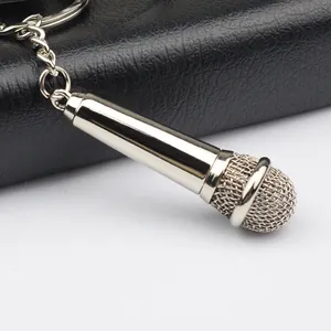 Polished silver microphone keychain with realistic metal mesh head on a dark leather surface