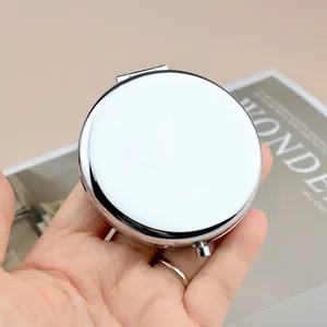 Sleek round silver metal pocket mirror for DIY gifts, held over a modern magazine background