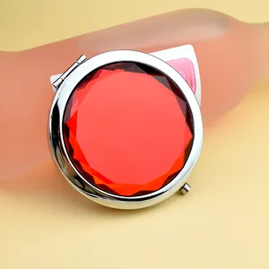 Portable round silver folding makeup mirror with a large faceted red gemstone top