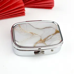 Portable mini metal pill box with marble pattern top on a white background with red fan