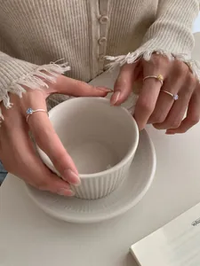 Detail von drei schmalen Silberringen mit bunten Zirkonia-Kristallen auf einer Tasse