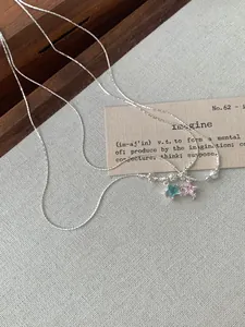 Détail de chaîne argentée avec pendentifs étoiles bleu clair et rose sur tissu texturé