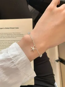 Detail of silver S925 starfish bracelet with pearl and blue bead on a model's wrist