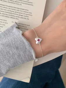 Detail of silver heart bracelet with a matte finish and square pink gemstone on wrist