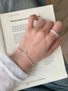 Close-up of a silver snake chain bracelet and a sparkling paved ring on a hand over a book
