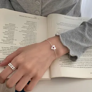 S925 silver heart bracelet with pink gemstone and woven ring on an open book
