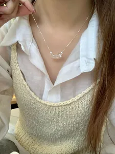 Détail du collier argenté avec perles œil-de-chat sur chemise blanche et gilet beige