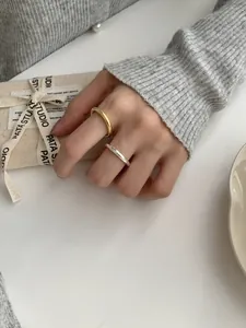 Minimalistische zilveren en gouden ringen gedragen door een model tegen een stoffen wand