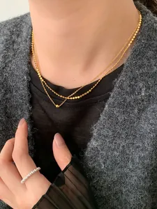 Dettaglio di una collana a doppio strato con sfere dorate e un anello a fascia in argento
