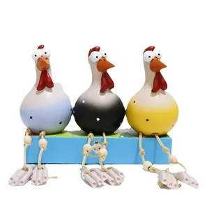 Three colorful resin big eye chicken figurines with rope legs sitting on a gift box