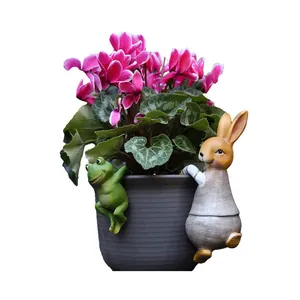 Garden frog and rabbit hanging resin statues on a flower pot with pink cyclamen