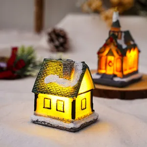 Dettaglio di casetta di Natale in resina luminosa con tetto innevato e luci LED