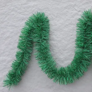 Green tinsel garland for Christmas decoration displayed in an S-shape on a gray background