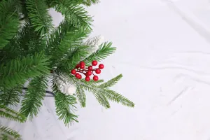 Detail of lush green Christmas tree branch with red berries and white flocked pinecones