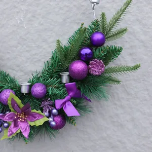 Künstlicher Weihnachtskranz mit lila Kugeln und Kiefernnadeln auf grauer Wand