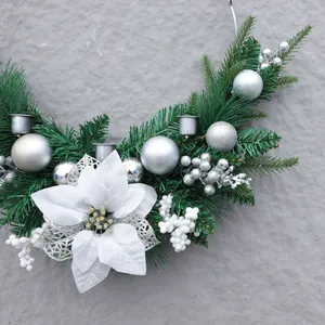 Silberner Weihnachtskranz mit Tannennadeln, Seidenblumen und Zapfen an grauer Wand