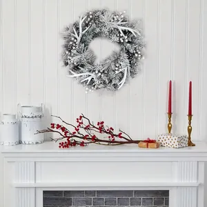 Winterlicher Weihnachtskranz mit beflocktem Geweih und roten Beeren am weißen Kamin