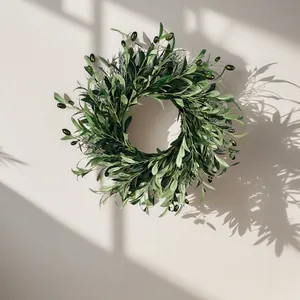 Artificial olive leaf wreath with green olives hanging on a neutral wall with shadows