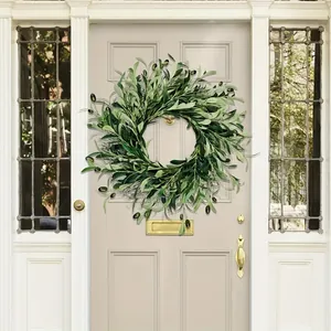 Artificial olive leaf wreath with black olives hanging on a neutral wooden door
