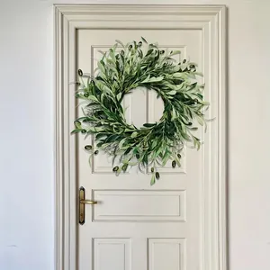 Artificial olive leaf wreath with green fruits hanging on a white wooden door