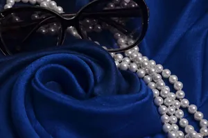Primer plano de gafas negras y collar de perlas multicapa sobre tela de seda lujosa