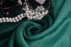 Detalle de bufanda de seda verde oscuro con textura ondulada, perlas y gafas