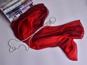 Primer plano de elegante bufanda de seda roja con perlas y revista de moda sobre blanco