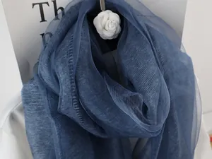 Close-up of a navy blue silk scarf with subtle pleats and a white camellia brooch