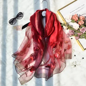 Detail of red silk scarf with floral embroidery and gold glitter hem on soft carpet