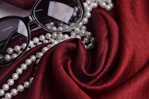 Detalle de la textura de bufanda de seda rojo oscuro con perlas y gafas vintage