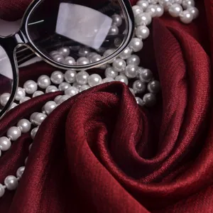 Primer plano de bufanda de seda rojo oscuro con collar de perlas y gafas de moda