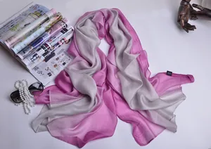 Detalle de bufanda de seda degradada rosa y gris con accesorios sobre fondo blanco