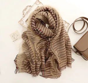 Close-up of silk scarf with houndstooth pattern, decorative tassels, and earthy tones