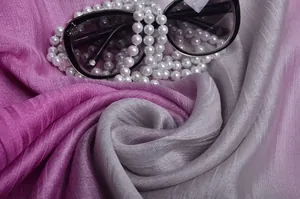 Detalle de bufanda de seda con degradado rosa a gris, collar de perlas y gafas
