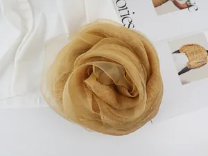 Detailed close-up of a layered ginger yellow silk flower brooch on a white satin shirt