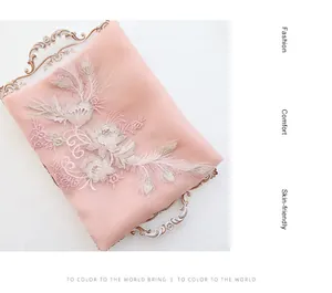 Close-up of pink silk wool scarf featuring intricate floral embroidery on a golden tray
