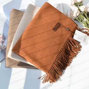 Detail of stacked cashmere-style scarves with fringe and premium leather logo labels