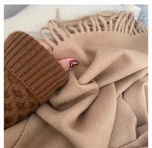 Close-up of khaki cashmere scarf with tassels layered on a chunky knit sweater