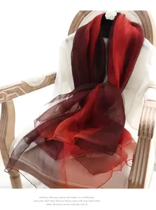 Gros plan d'une écharpe élégante en soie dégradé rouge sur une chaise en bois