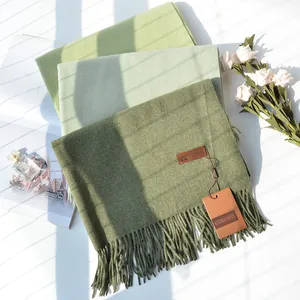 Detailed close-up of three green cashmere-like scarves with fringes and brand tags