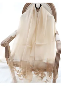 Detail of beige silk wool shawl with elegant gold floral embroidery on light fabric