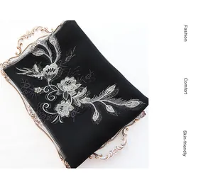 Detail of silver floral embroidery on black silk wool scarf displayed in a gold vintage tray