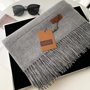 Solid gray cashmere-feel scarf with tassels and brand tag on a tray with accessories